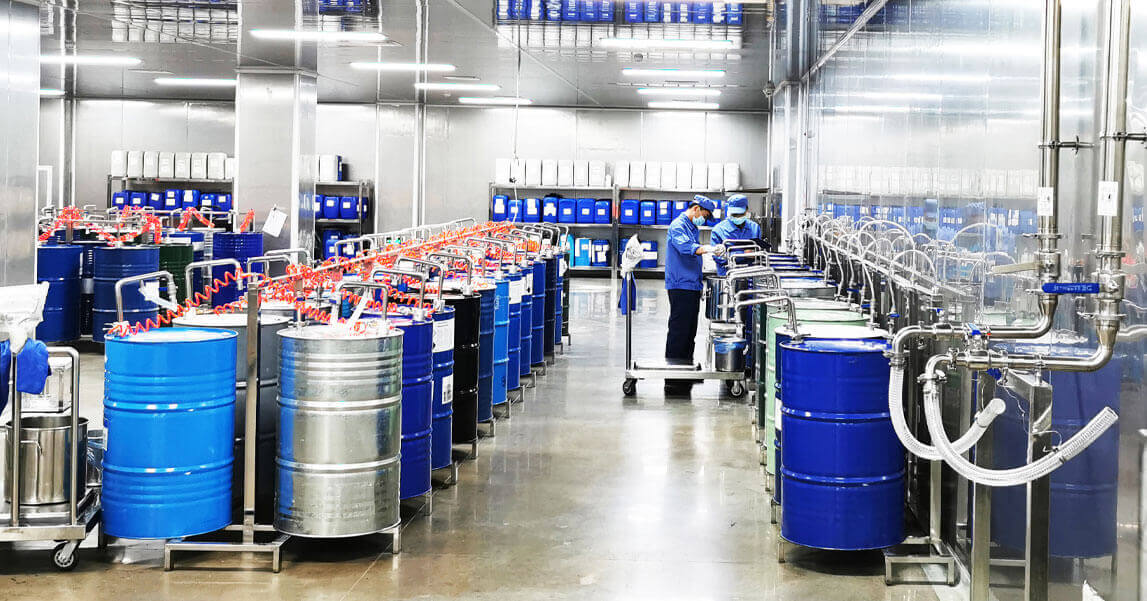 Workers operating a liquid flavor production floor with stainless-steel piping and food-grade drums