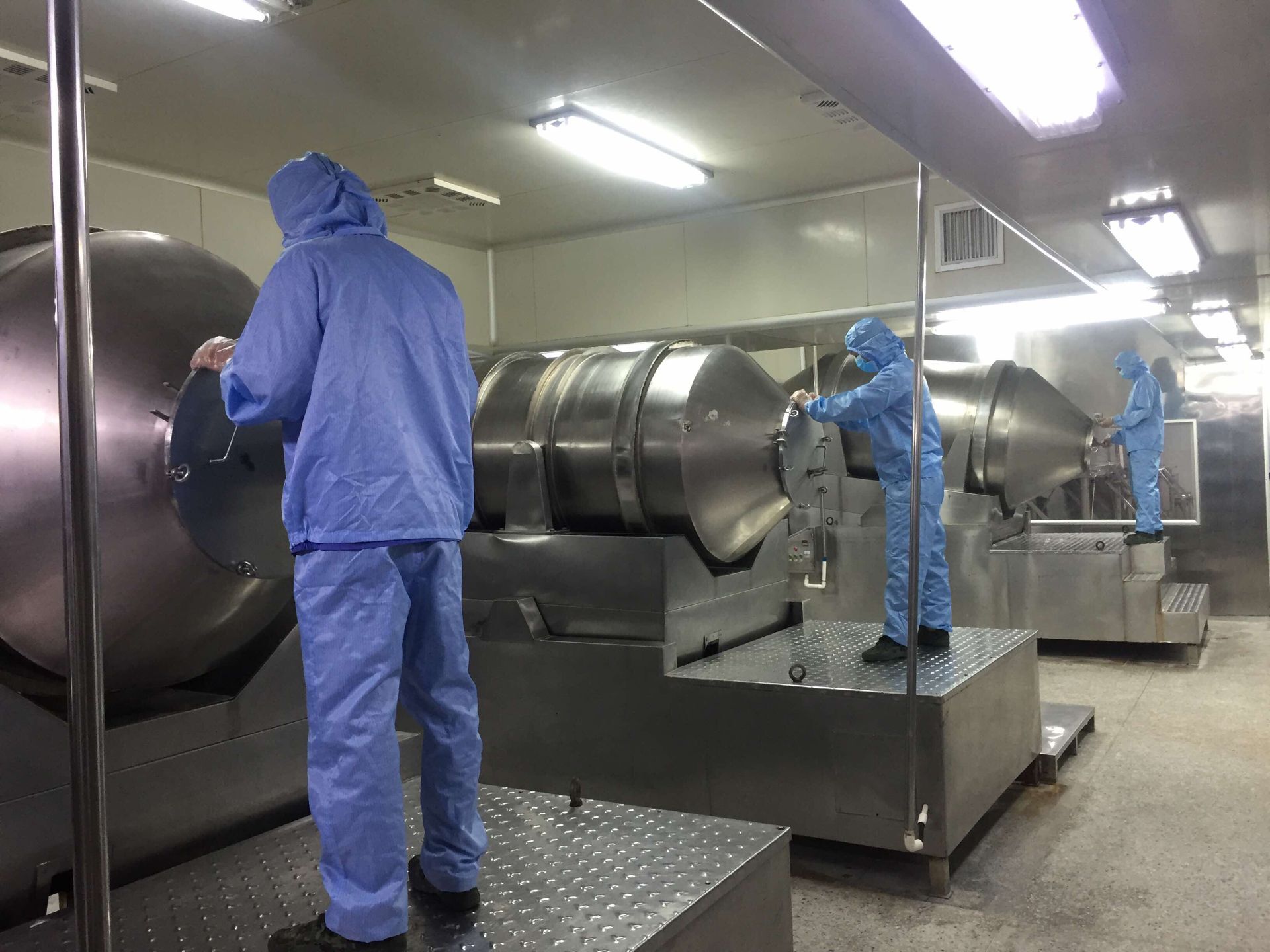 Production team operating enclosed stainless-steel rotary blending equipment